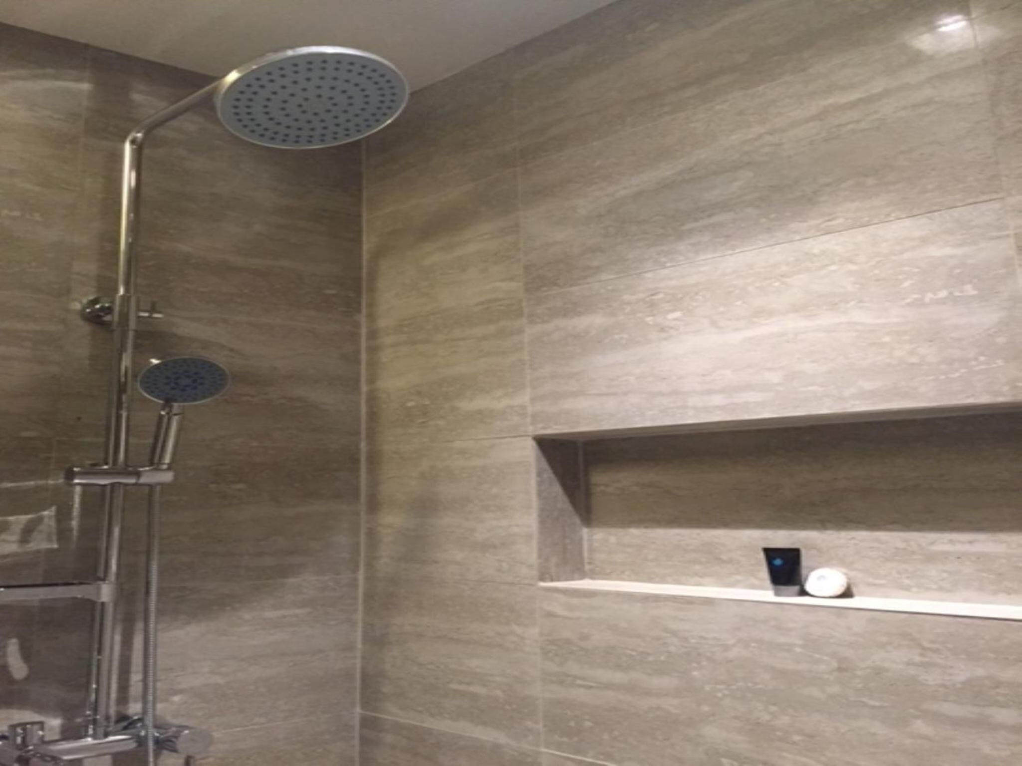 A modern bathroom with a walk-in shower, a handheld showerhead, and a wall-mounted control panel.
