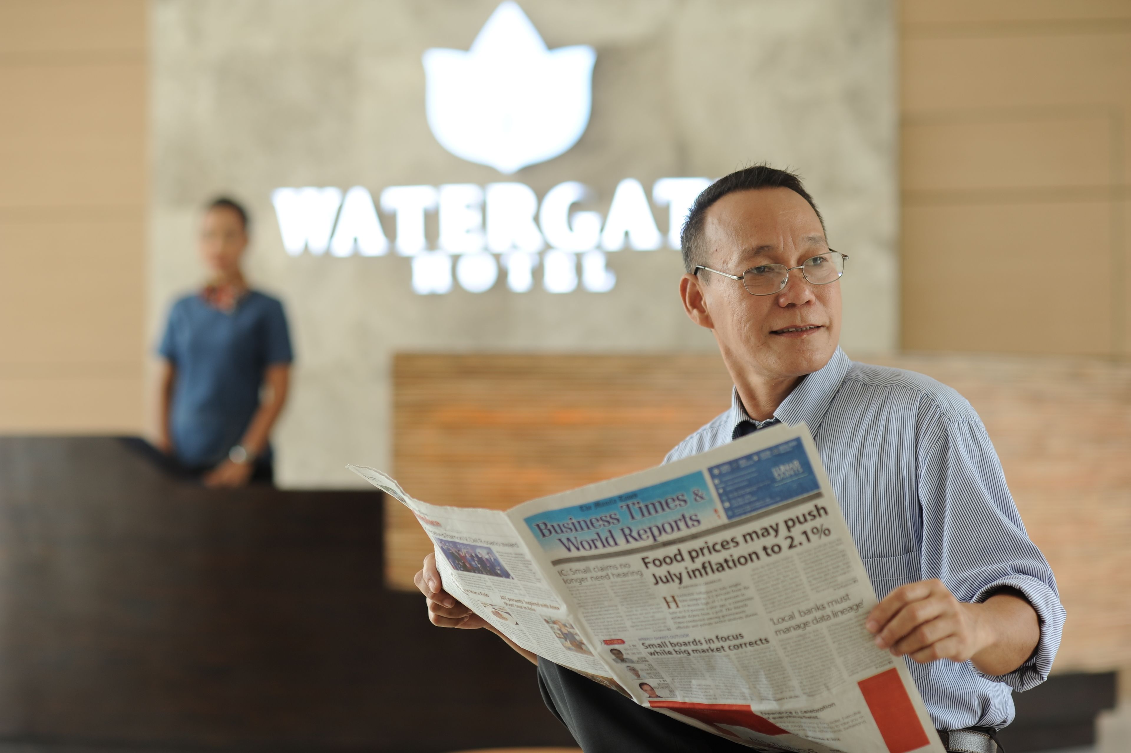A person reading a newspaper in front of a Watergate Hotel sign.
