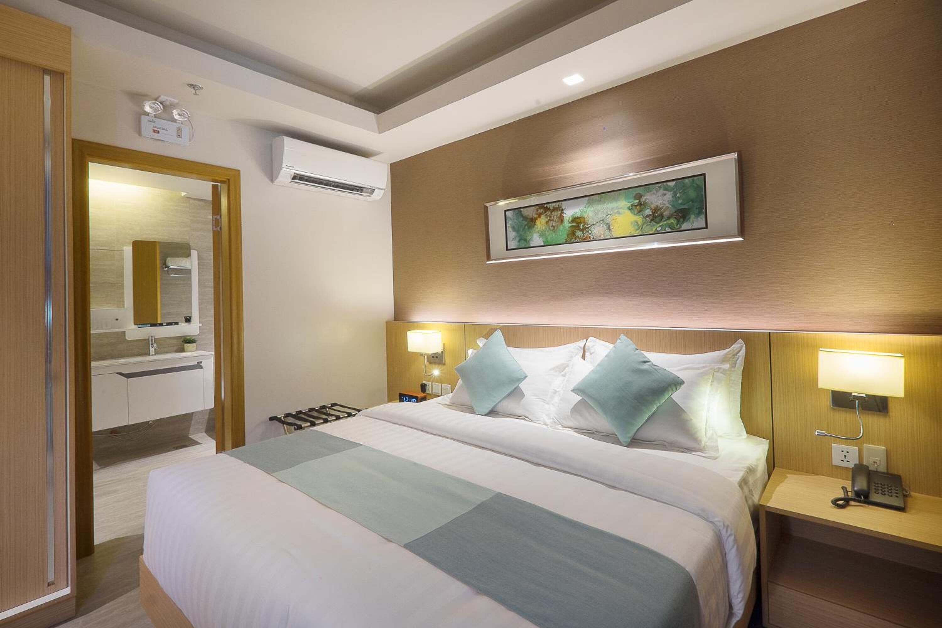 Une chambre d’hôtel avec un grand lit, des tables de chevet, un miroir, un appareil de climatisation et un tableau au mur.