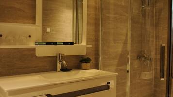Un baño moderno con ducha envuelta en vidrio, tocador blanco con espejo y una planta pequeña sobre el mostrador.