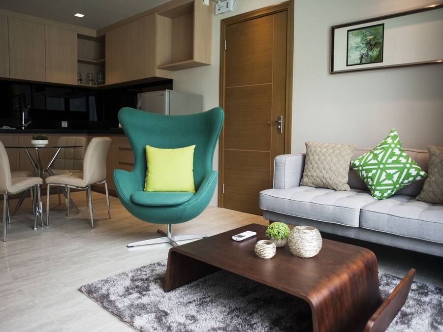 A modern living room with a teal armchair, a grey sofa, and a wooden coffee table.