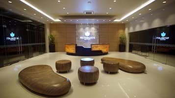 Welcome to the Watergate Hotel, where guests can relax in the stylish lobby featuring a central reception desk, round seating areas, and potted plants.