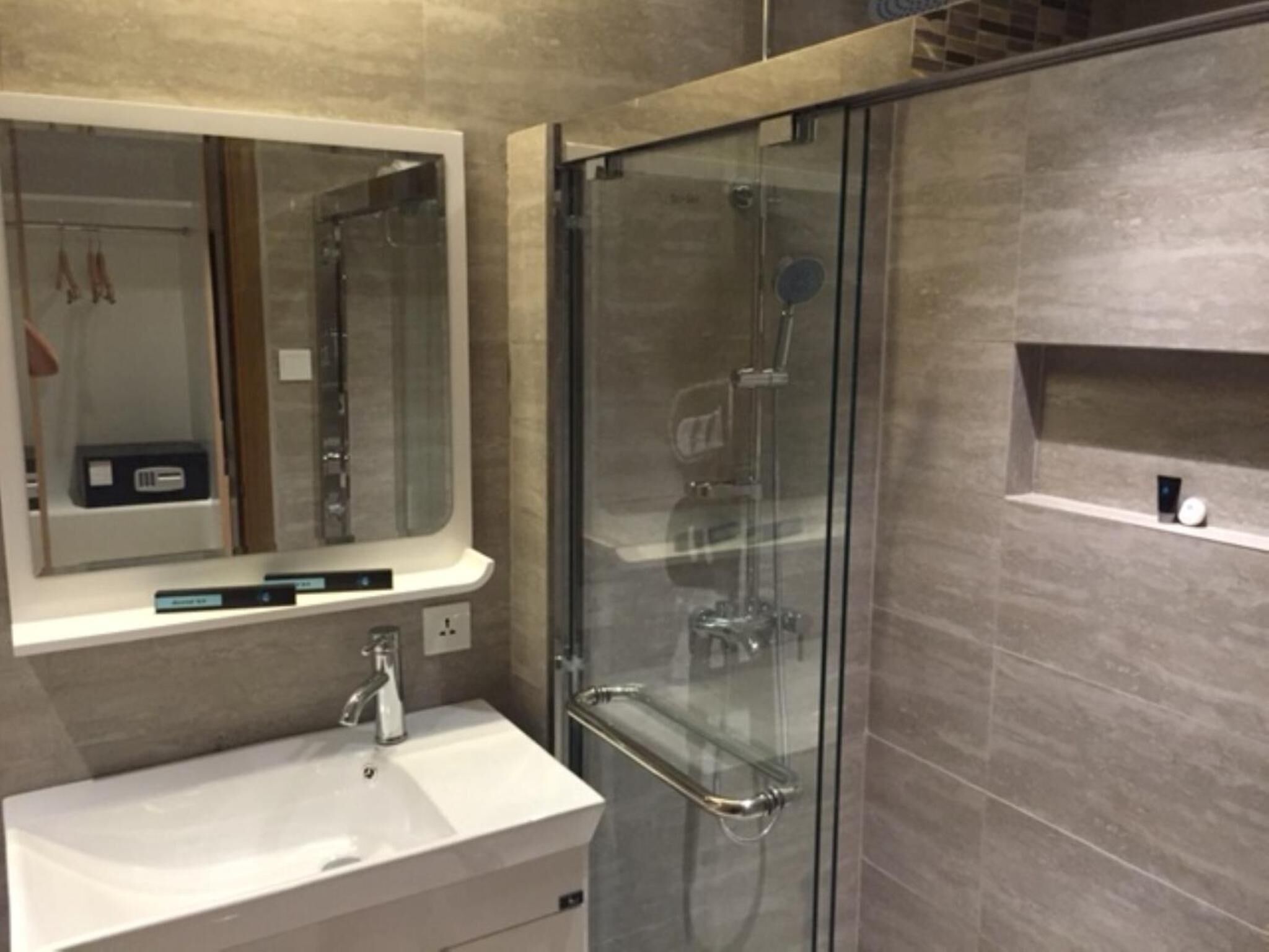 A modern bathroom with a glass-enclosed shower, a white sink, and a mirror above the sink.