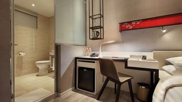 Habitación de hotel compacta con ducha, inodoro, escritorio, silla y cama.