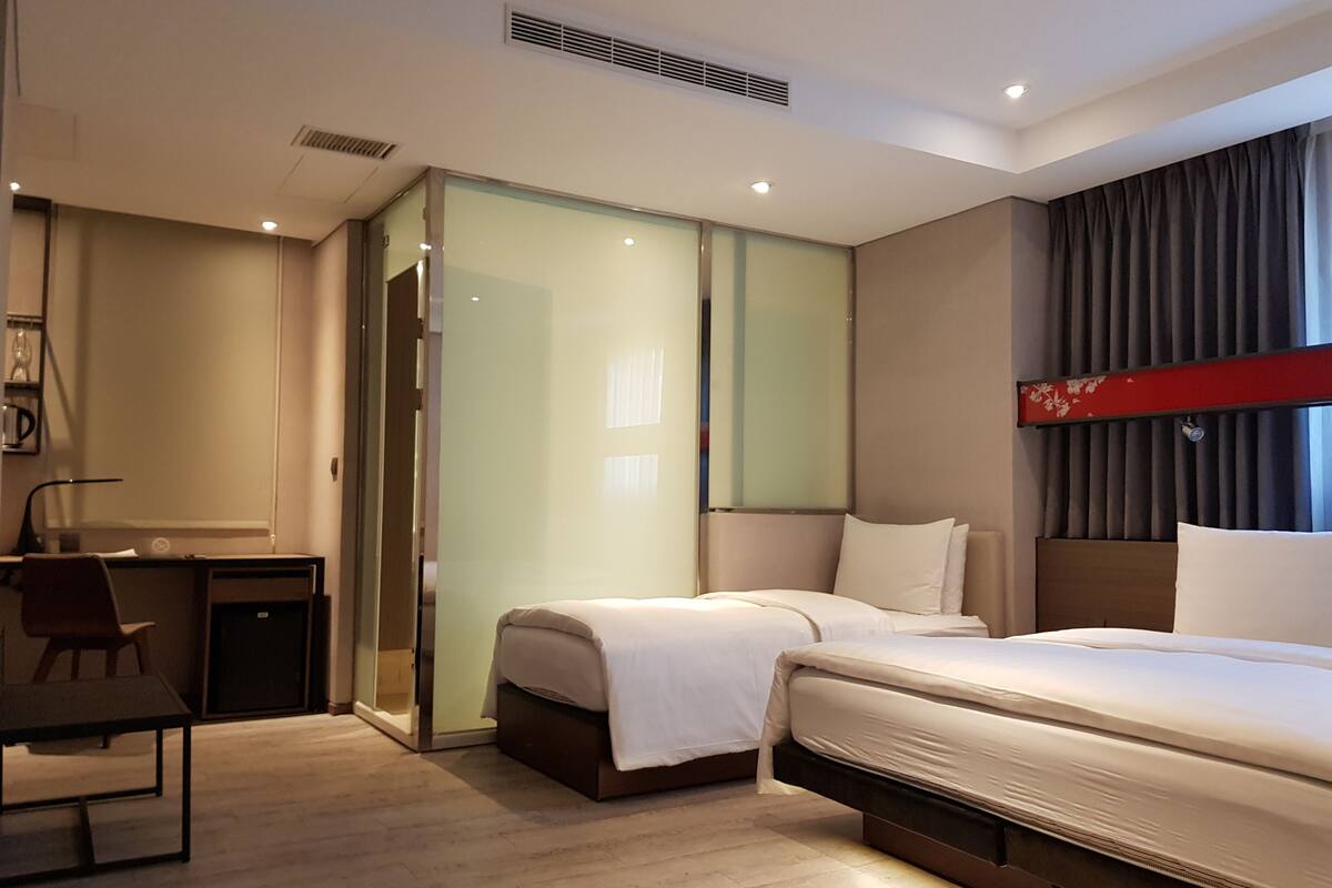 Ein modernes Hotelzimmer mit Bett, Schreibtisch und Stuhl. Eine Schiebetür führt zum Badezimmer.