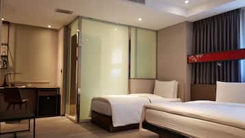 A modern hotel room with a bed, a desk, and a chair. There is a sliding door leading to a bathroom.