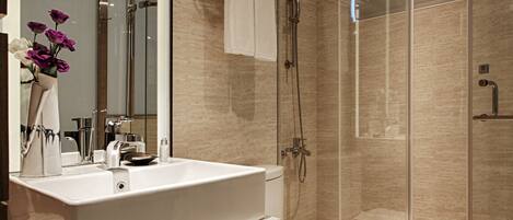 A modern bathroom with a large mirror, a white sink, a toilet, and a glass-enclosed shower area.