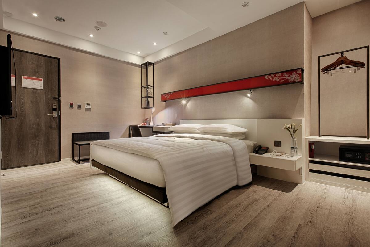 Ein modernes Hotelzimmer mit einem großen Bett, Nachttischen, einem Schreibtisch und einem Kleiderschrank.