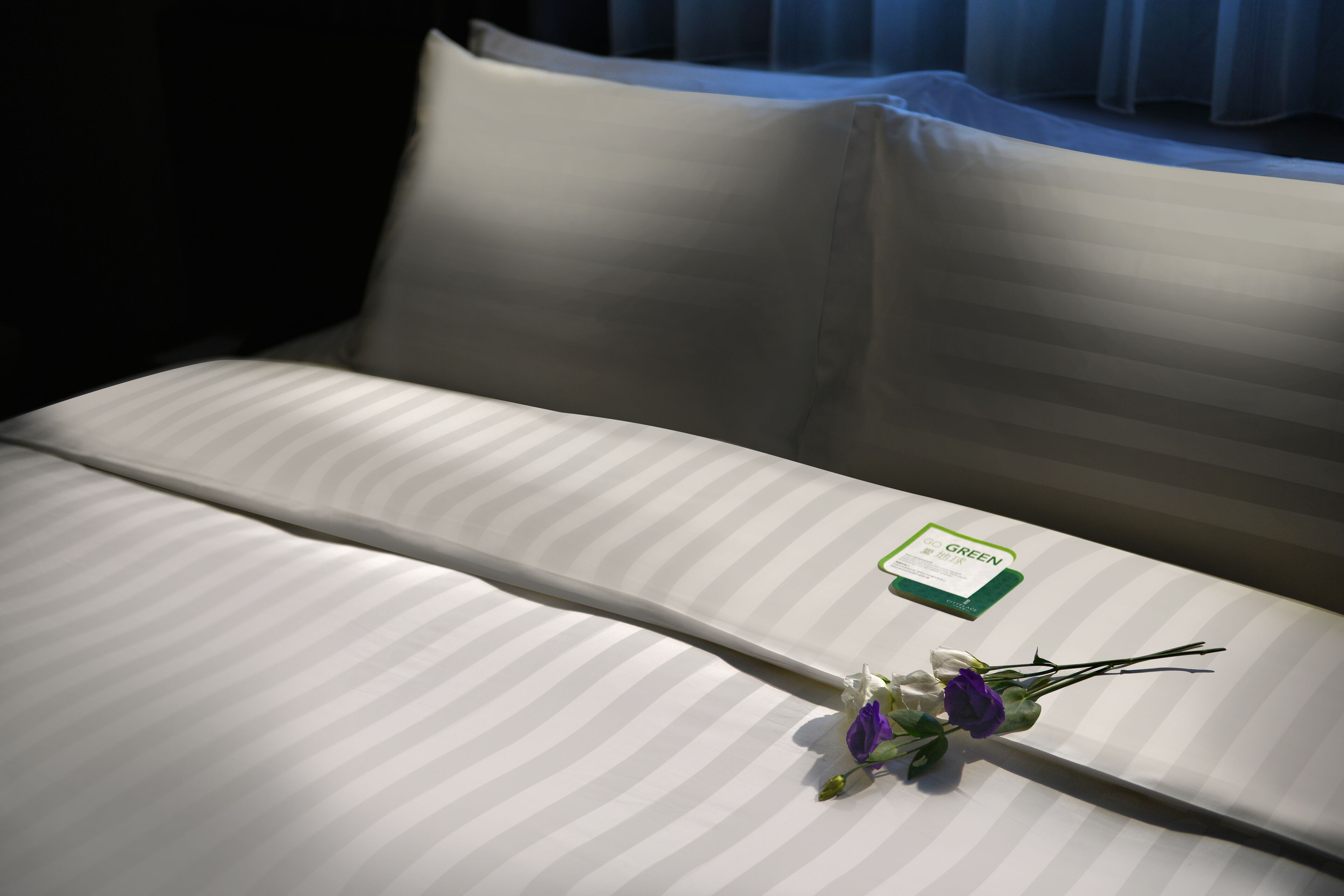 A neatly made bed with a green card and a bouquet of flowers.