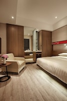 A modern hotel room with a bed, a seating area, a vanity, and a mirror.