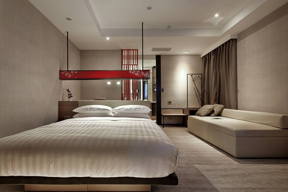Ein modernes Schlafzimmer mit einem großen Bett, einer Couch und einer roten Dekowa Wandfläche.