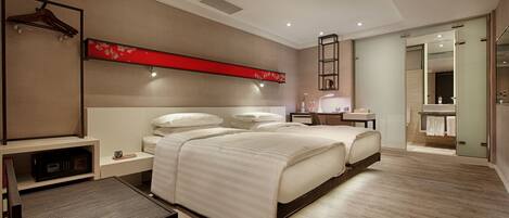 Una habitación de hotel moderna con dos camas, un escritorio, una silla, un panel decorativo rojo y un baño con espejo y toallero.