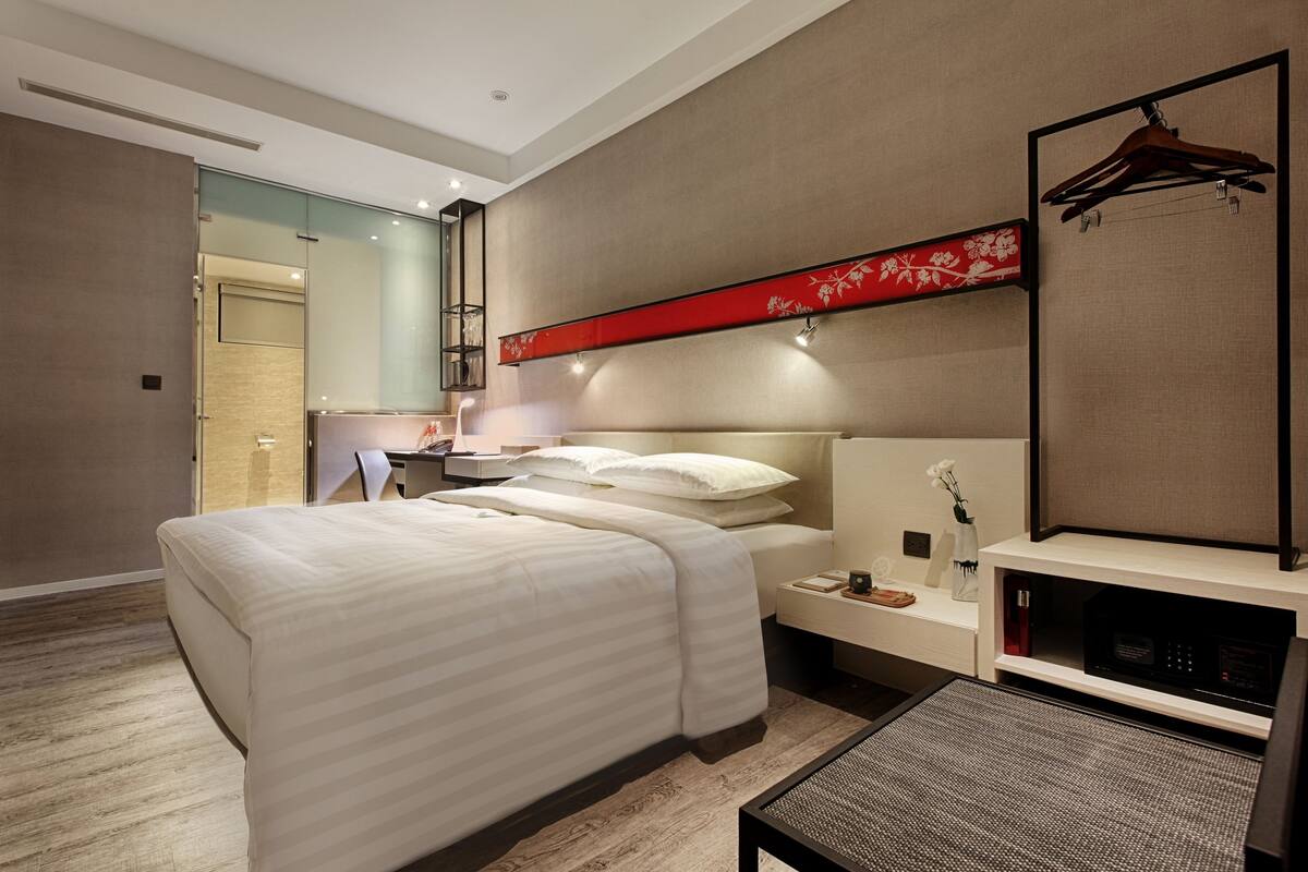 Ein modernes Hotelzimmer mit einem großen Bett, Nachttischen, einem Fernseher und einer roten Zierteilung.