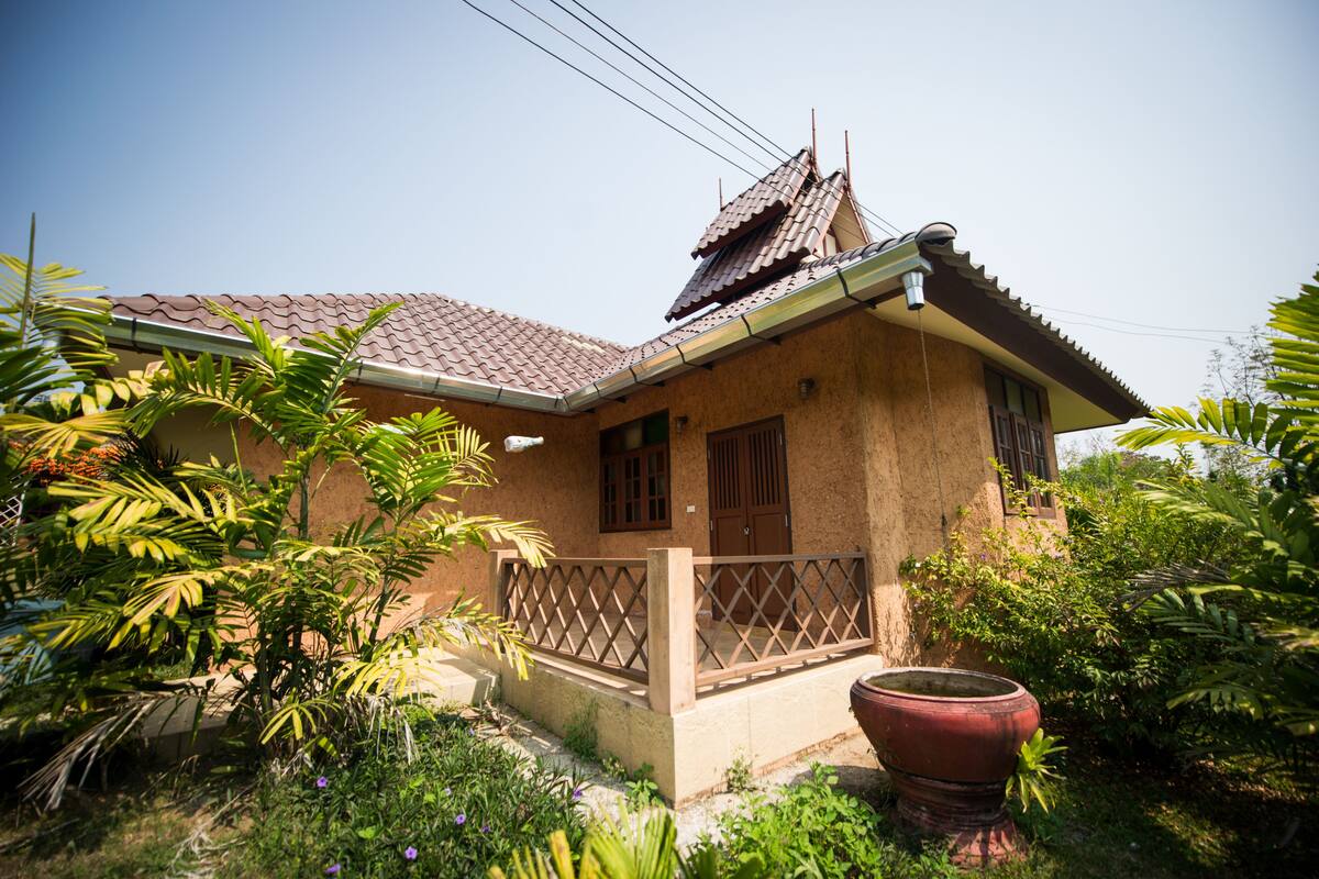 A house with a tiled roof, a balcony with a lattice railing, and a large potted plant in the yard.