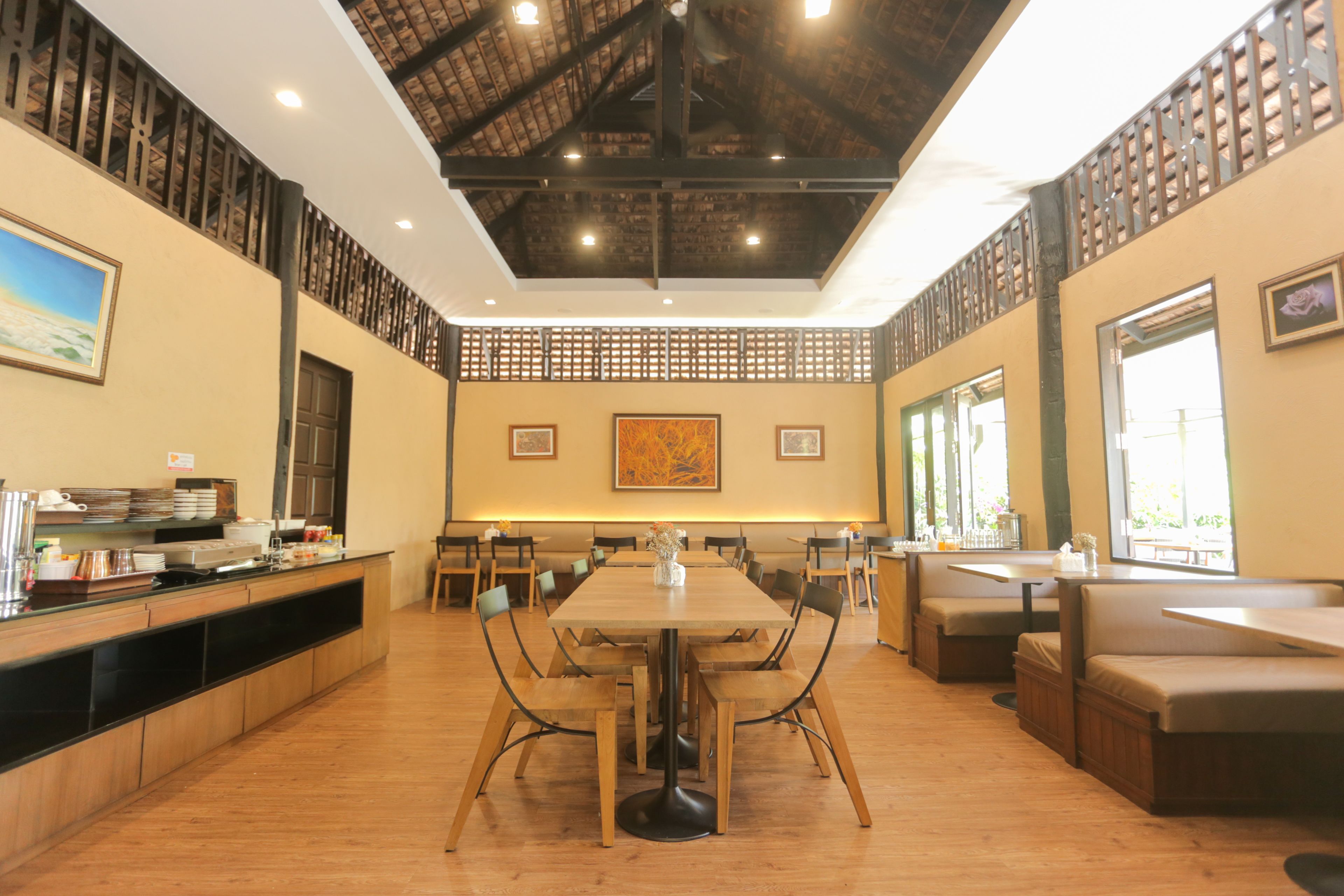 A spacious dining area with a long wooden table surrounded by chairs, a high ceiling with exposed beams, and large windows allowing natural light.