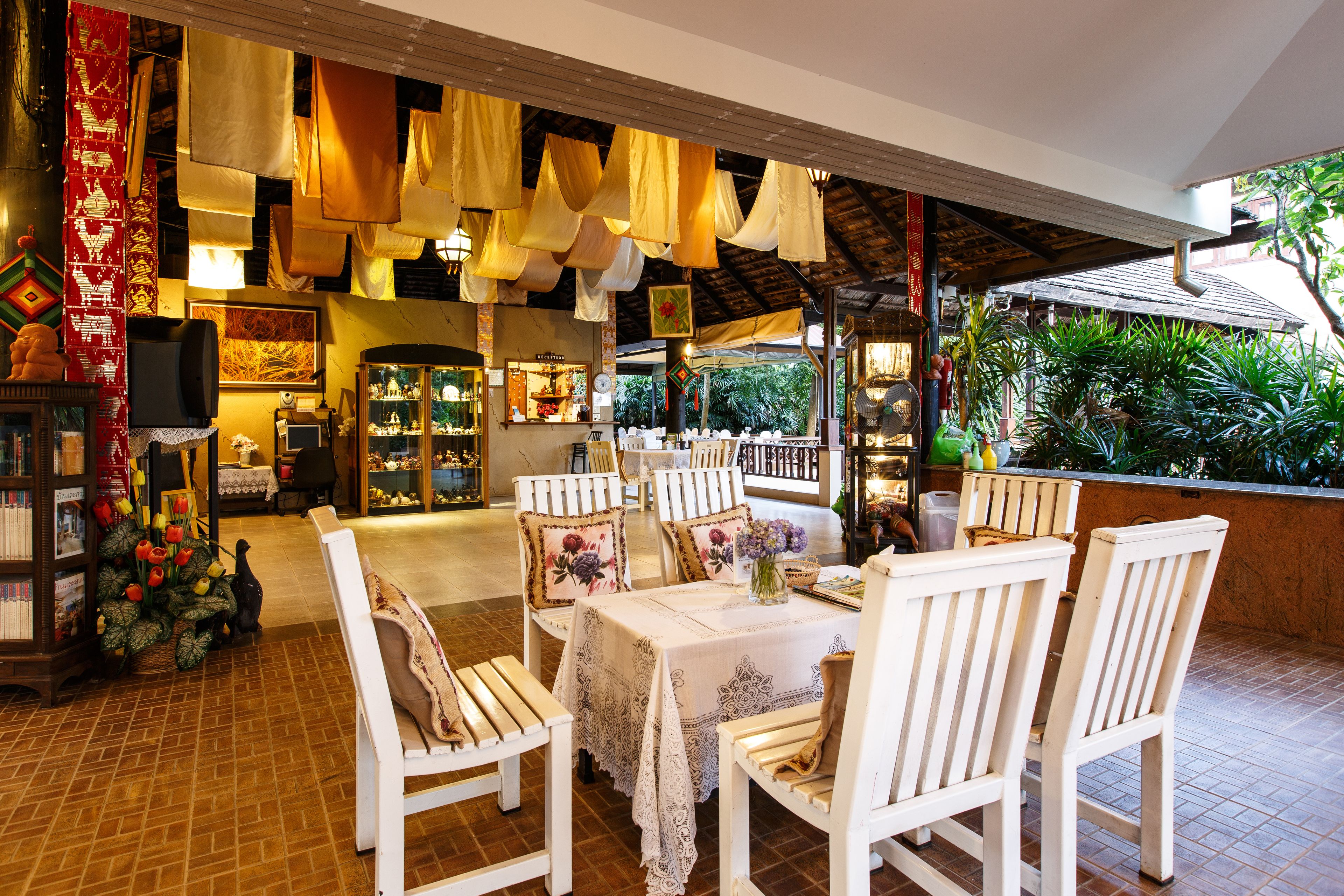 A restaurant with white wooden chairs and tables, hanging fabrics, and a tiled floor.