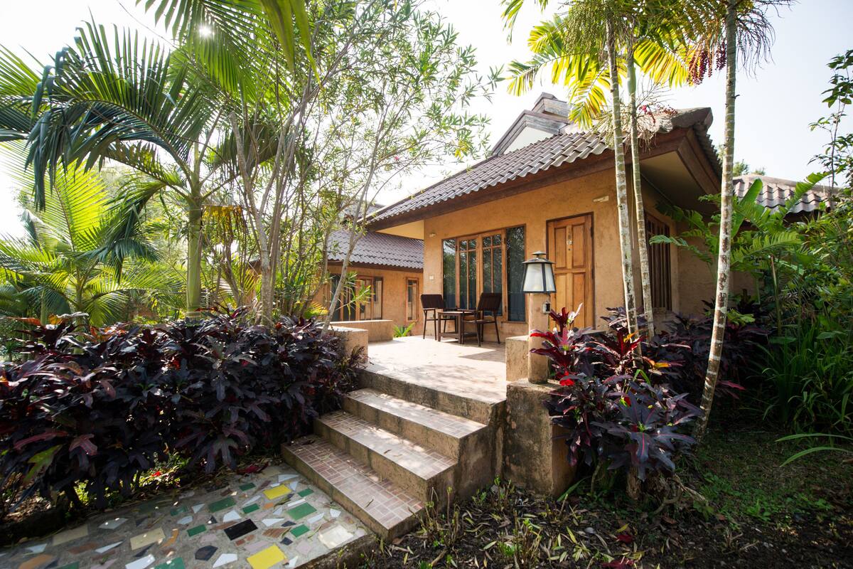 A house with a tiled patio, a small table and chairs, and a staircase leading to the entrance.