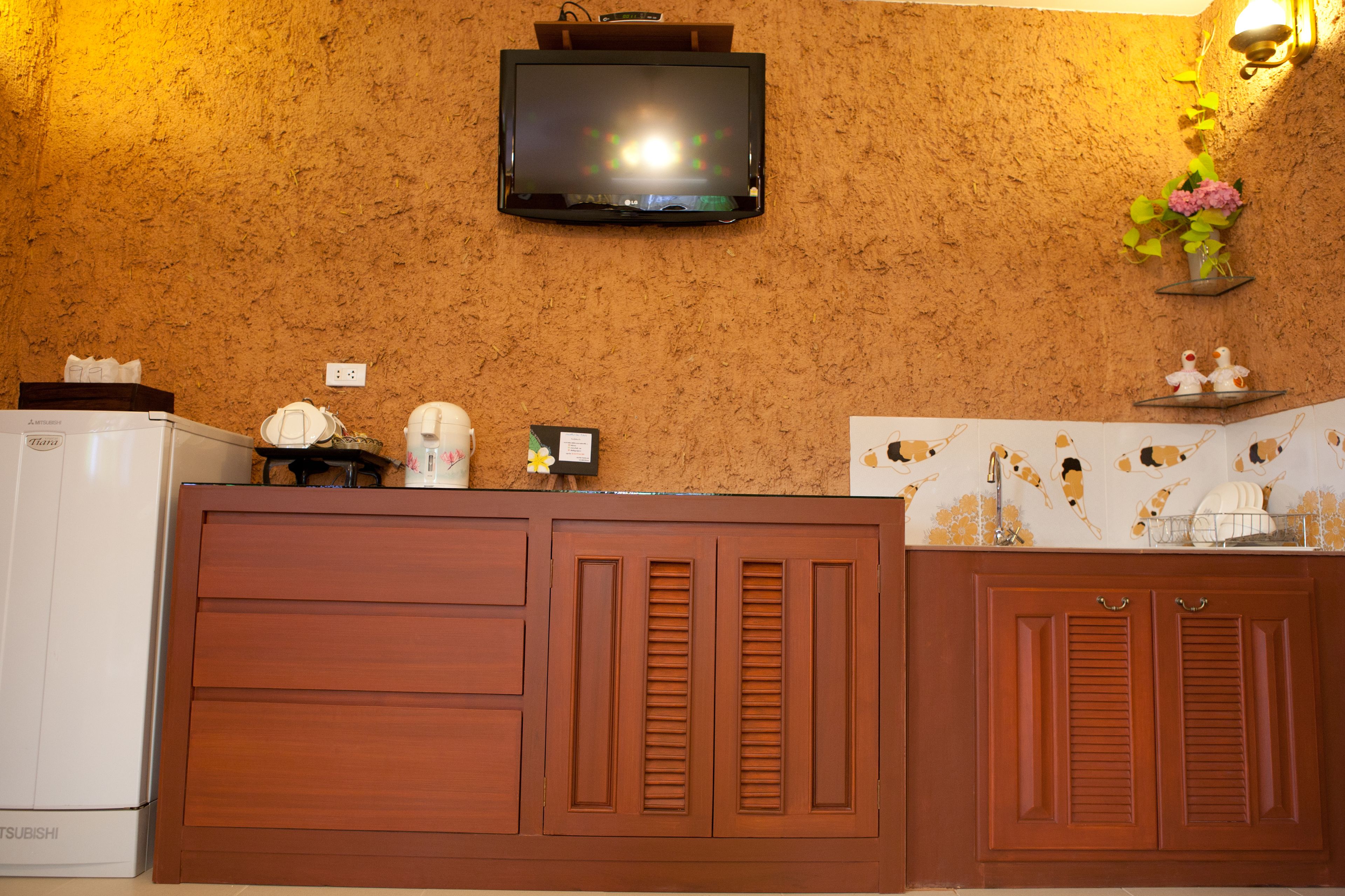 A kitchen with wooden cabinets, a white refrigerator, a mounted television, and decorative items on the wall.