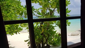Une vue sur une plage, avec son eau turquoise et son sable blanc, le tout encadré par un feuillage verdoyant et luxuriant, telle qu'on peut l'admirer depuis une fenêtre.