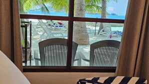 Une chambre d’hôtel avec un lit, une fenêtre donnant sur la plage et les palmiers, et une serviette pliée posée sur le lit.