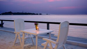 Une vue sur la mer avec une table et deux chaises, un vase de fleurs et une rambarde.
