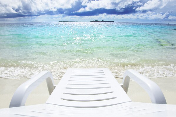 Une vue sur la plage, avec une chaise longue blanche et une petite île au loin.