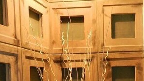 Un grand vase orné de branches est posé sur une table dans une pièce où se trouvent des meubles en bois.