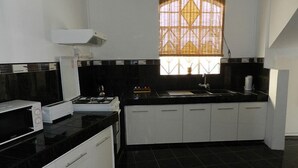 Une cuisine moderne avec des plans de travail noirs, des meubles blancs, une cuisinière à gaz et une fenêtre agrémentée de stores à motifs.