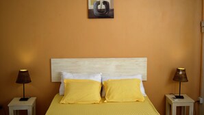 Une chambre d’hôtel avec une tête de lit en bois, deux lampes de chevet, un lit avec une literie jaune et un tableau au-dessus du lit.