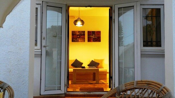 Un intérieur chaleureux avec un canapé et des coussins, un luminaire suspendu et une vue à travers une porte vitrée.