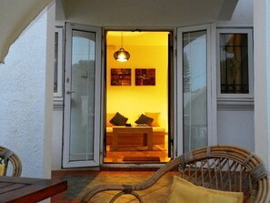 Un intérieur chaleureux avec un canapé et des coussins, un luminaire suspendu et une vue à travers une porte vitrée.