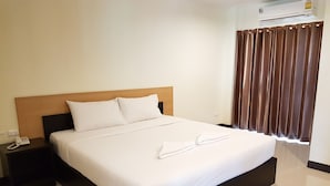 A hotel room with a large bed, a wooden headboard, a bedside table with a phone, and a window with brown curtains.