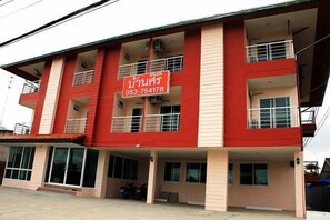 A multi-story building with a red and beige facade, balconies, and a sign with a phone number.