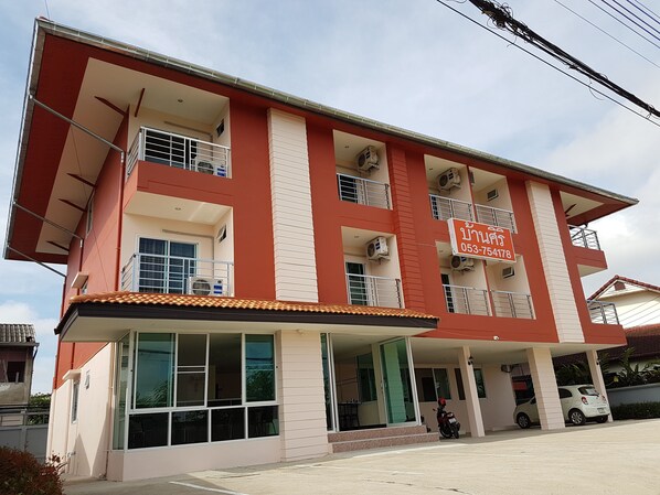 A multi-story building with a red and white facade, large windows, and a sign with a phone number.