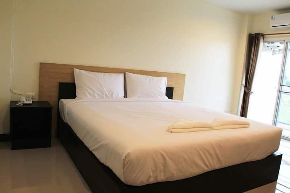 Cama bem arrumada com lençóis brancos e toalha dobrada, mesa de cabeceira com telefone e janela com cortinas.