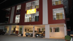 A multi-story building with a prominent yellow sign displaying a phone number. There are two cars parked in front, and the building has large windows and balconies.
