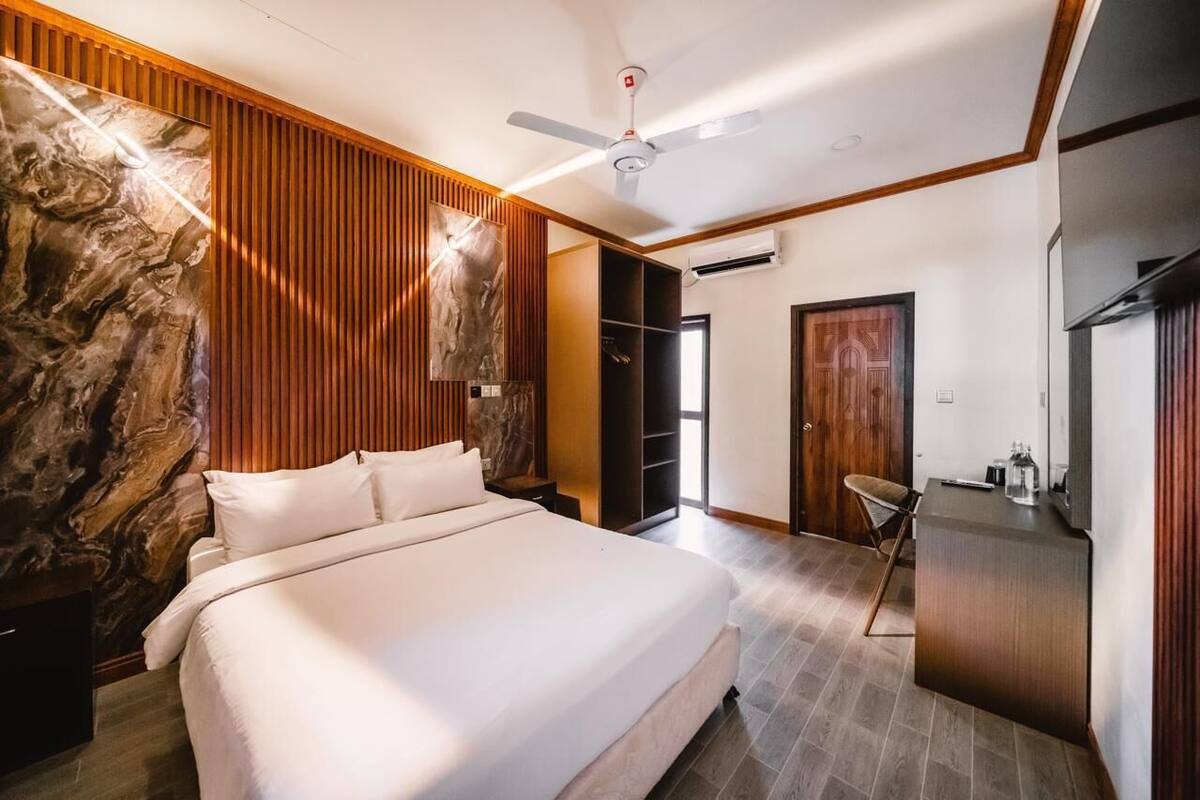 A modern bedroom with a large bed, wooden paneling, a ceiling fan, and a desk area.