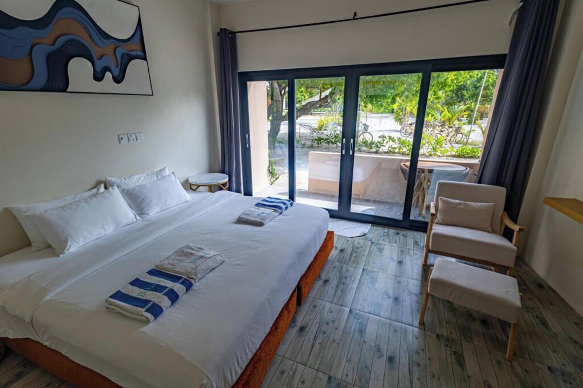 A hotel room with a large bed, a small round table, a chair, and a view of the outdoors through a sliding glass door.