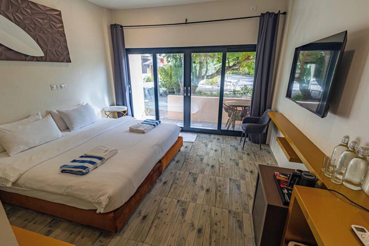 A hotel room with a large bed, a desk with a chair, a TV, and a balcony with a view of the street.