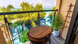 A balcony with a wooden table and chairs, overlooking a pool and tropical vegetation. - Bibee Maldives (Dhiffushi)