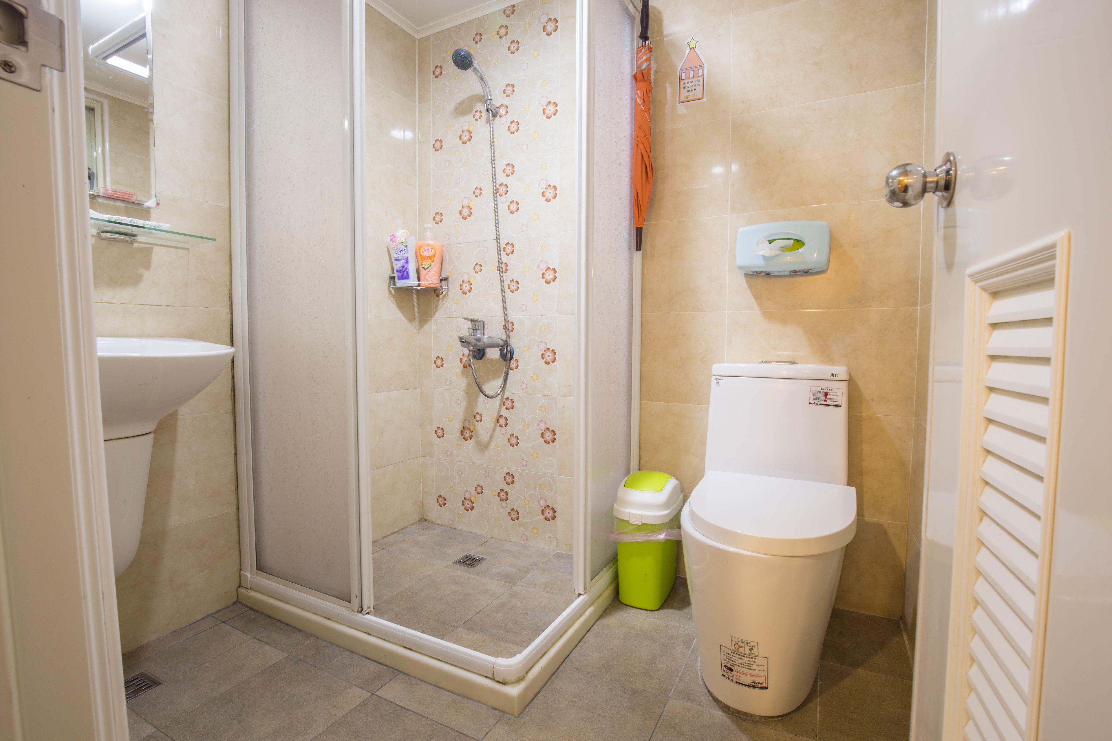 A bathroom with a shower, toilet, sink, and a trash bin.