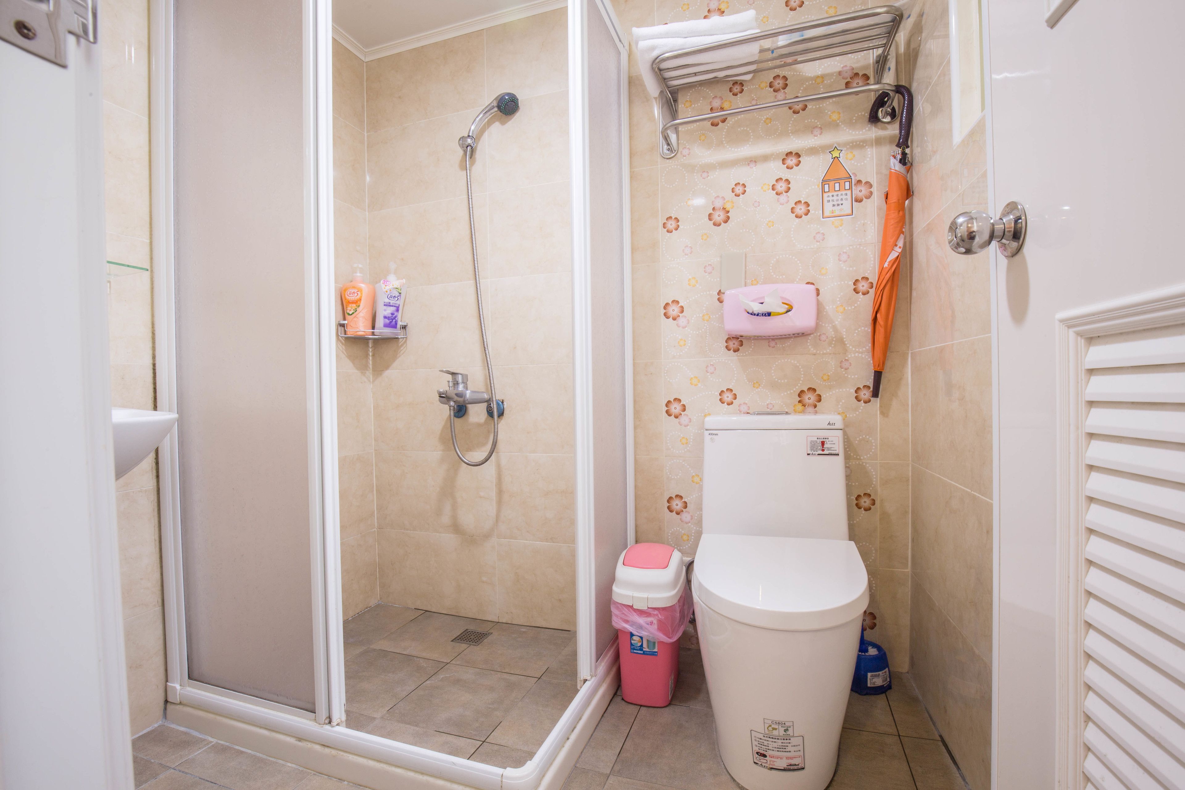 A bathroom with a shower, toilet, and a small trash bin.