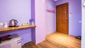Un couloir avec un plancher en bois, une porte en bois, une étagère avec une bouilloire, une bouteille d’eau et une boîte.