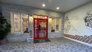 Une entrée d’immeuble avec une porte rouge, une façade en pierre et un sol carrelé.