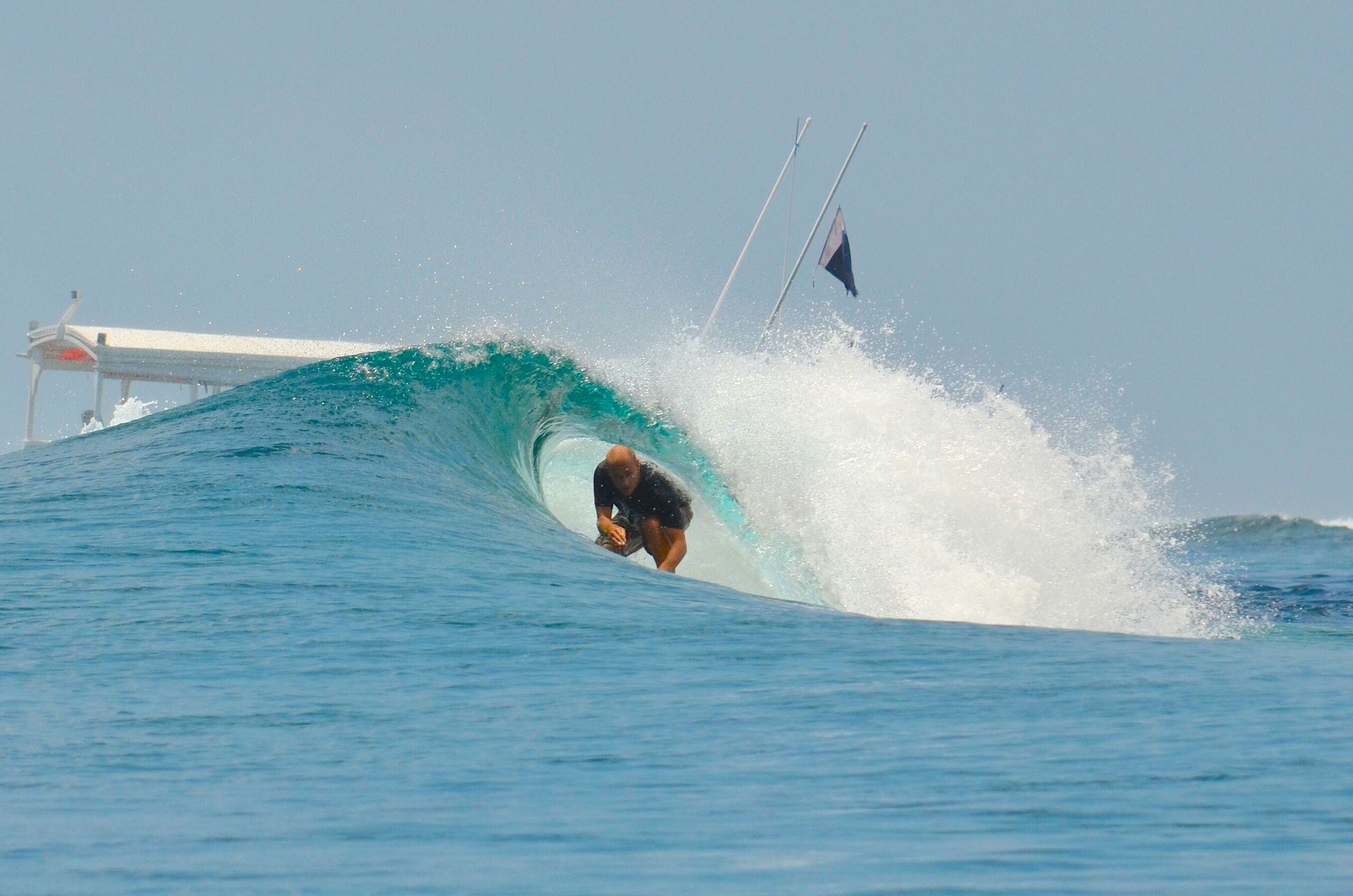 A surfer riding a wave with a boat in the background.