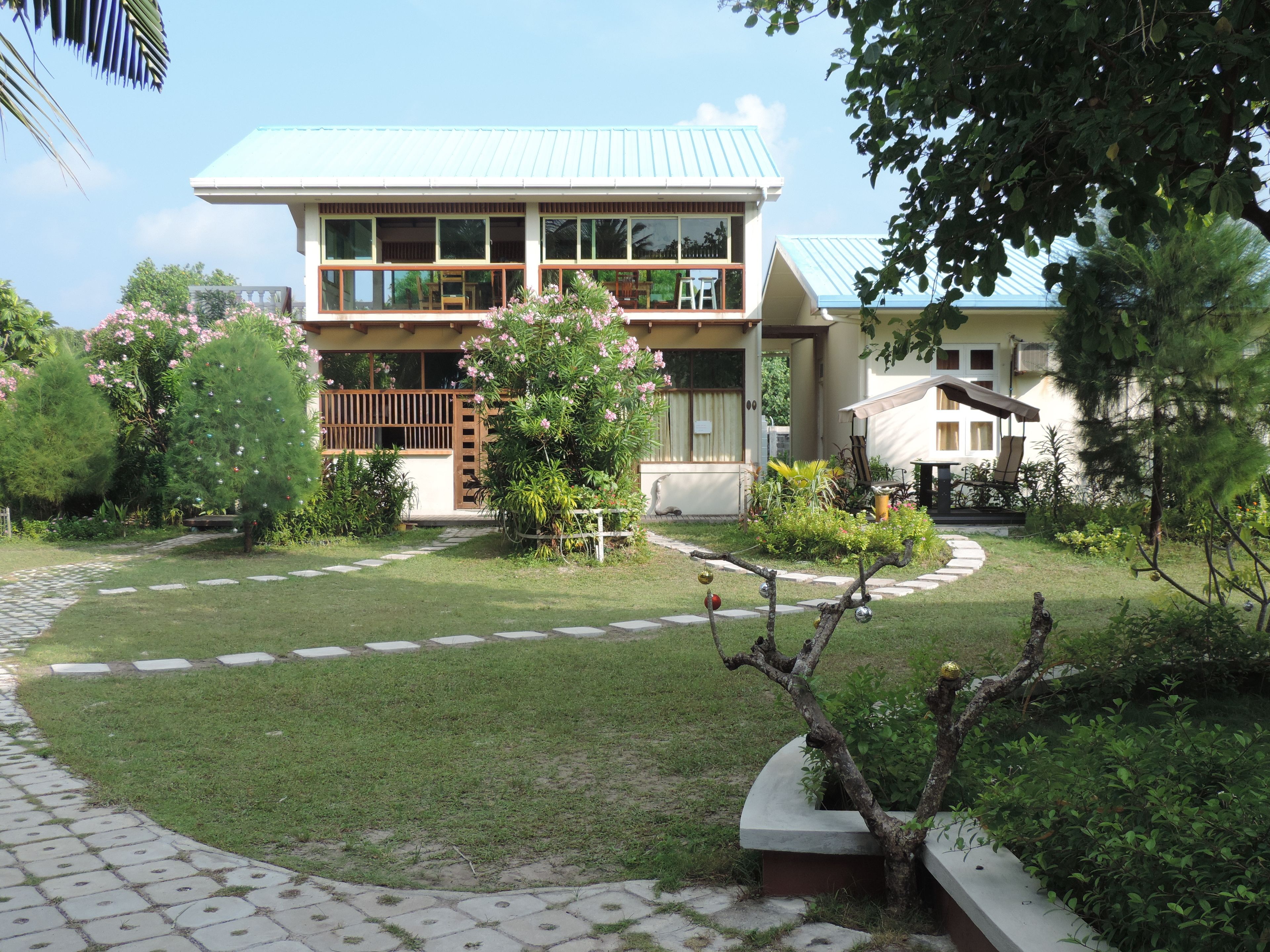 A two-story building with a flat roof, surrounded by a well-maintained garden with a paved walkway.