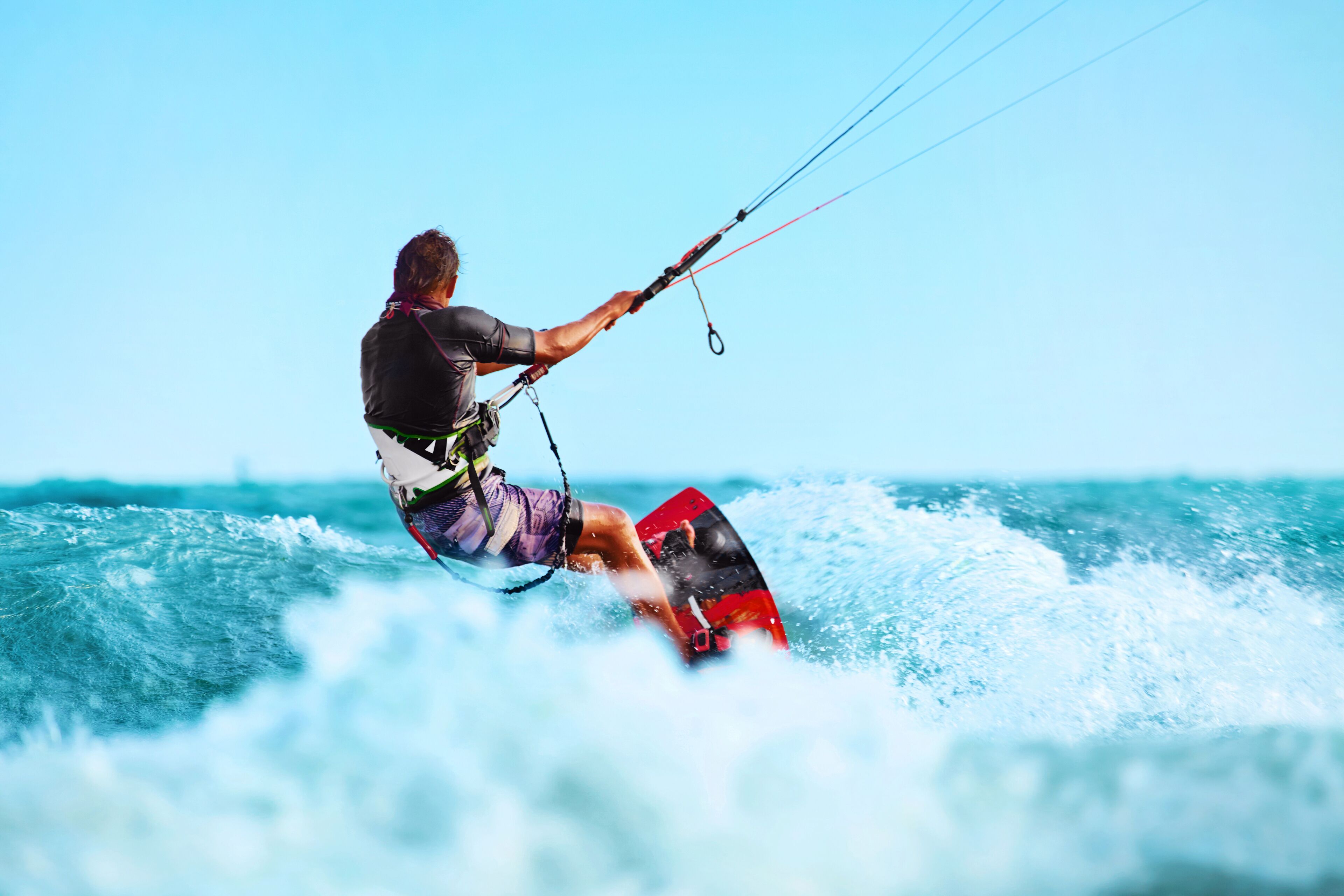 Una persona practica windsurf en un tabla roja en el océano.