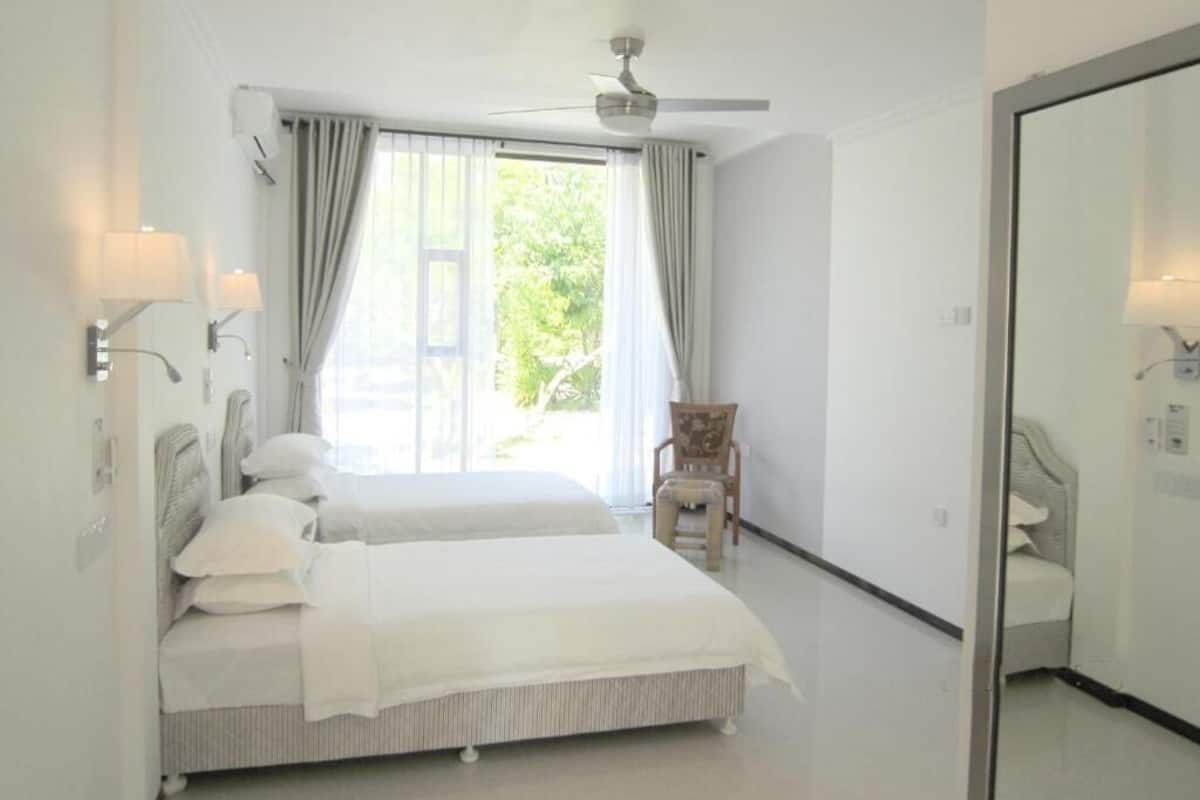 A hotel room with two beds, a ceiling fan, a chair, and a large mirror.