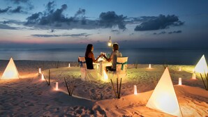 Una pareja cenando en una mesa frente al mar, con vista a las dunas de arena.