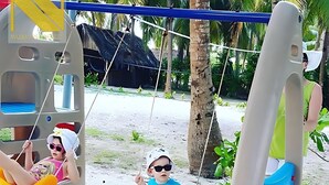 Una playa con columpios y una cabaña con techo de paja al fondo.